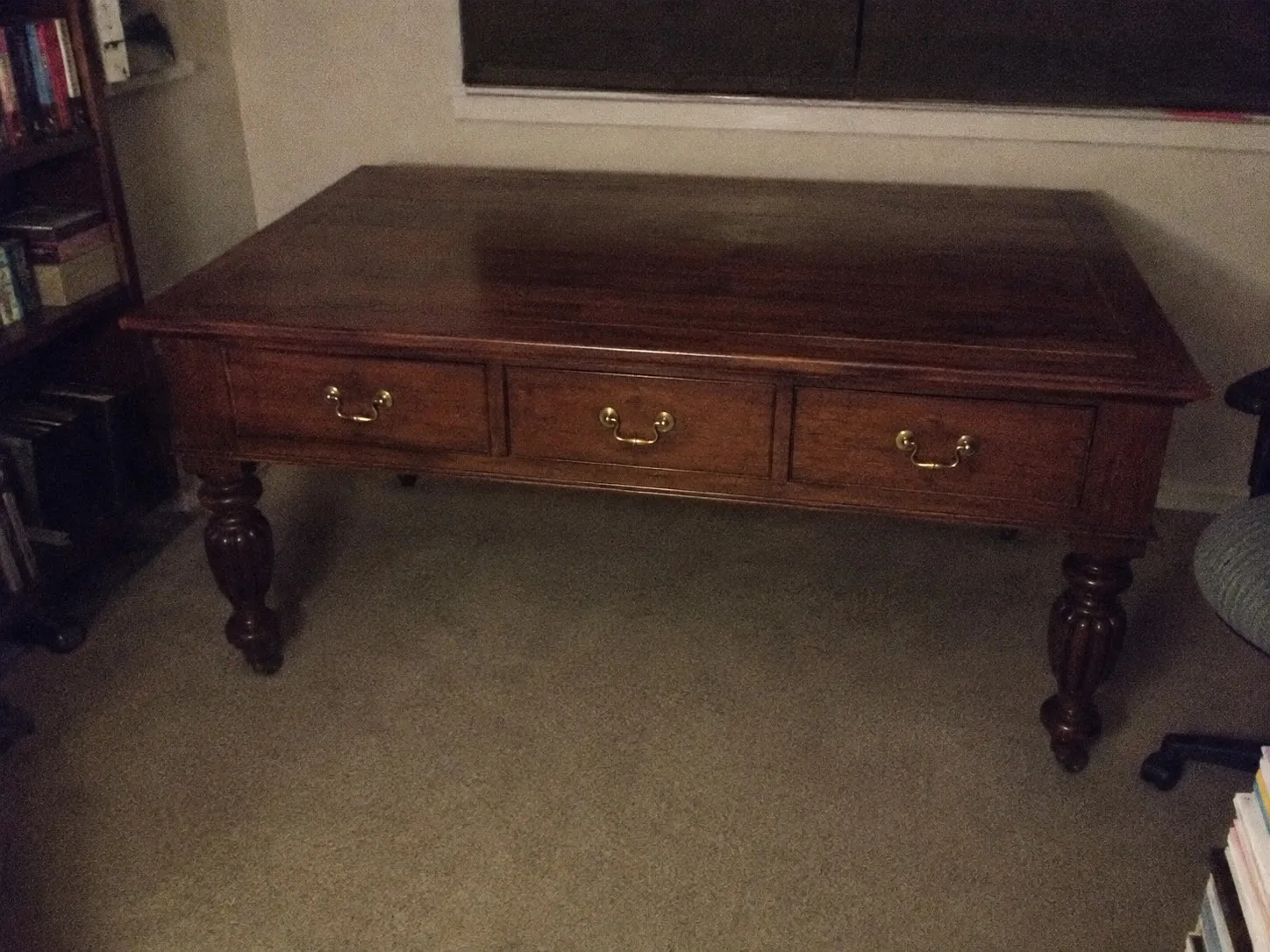 An antique writing table photographed in a dim study, the room light off