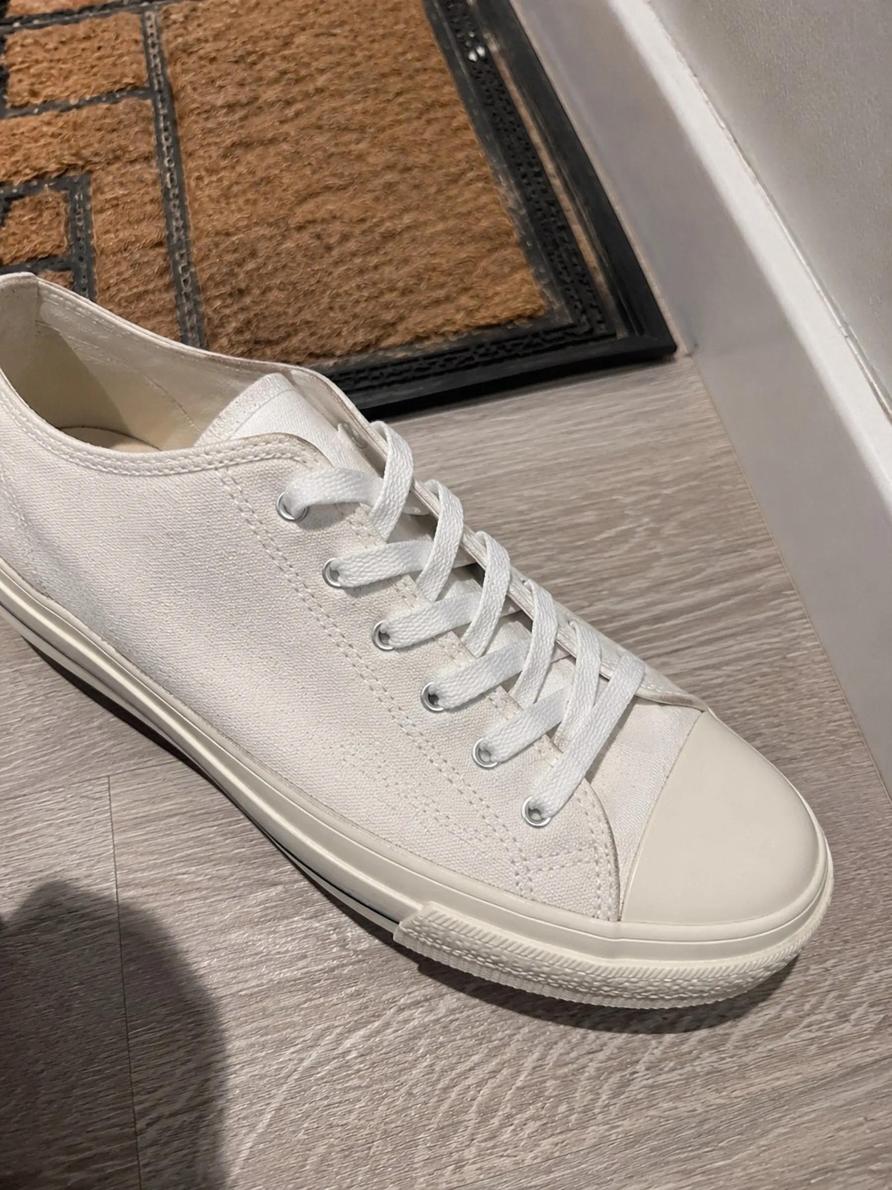A white canvas sneaker photographed on the floor by the front door