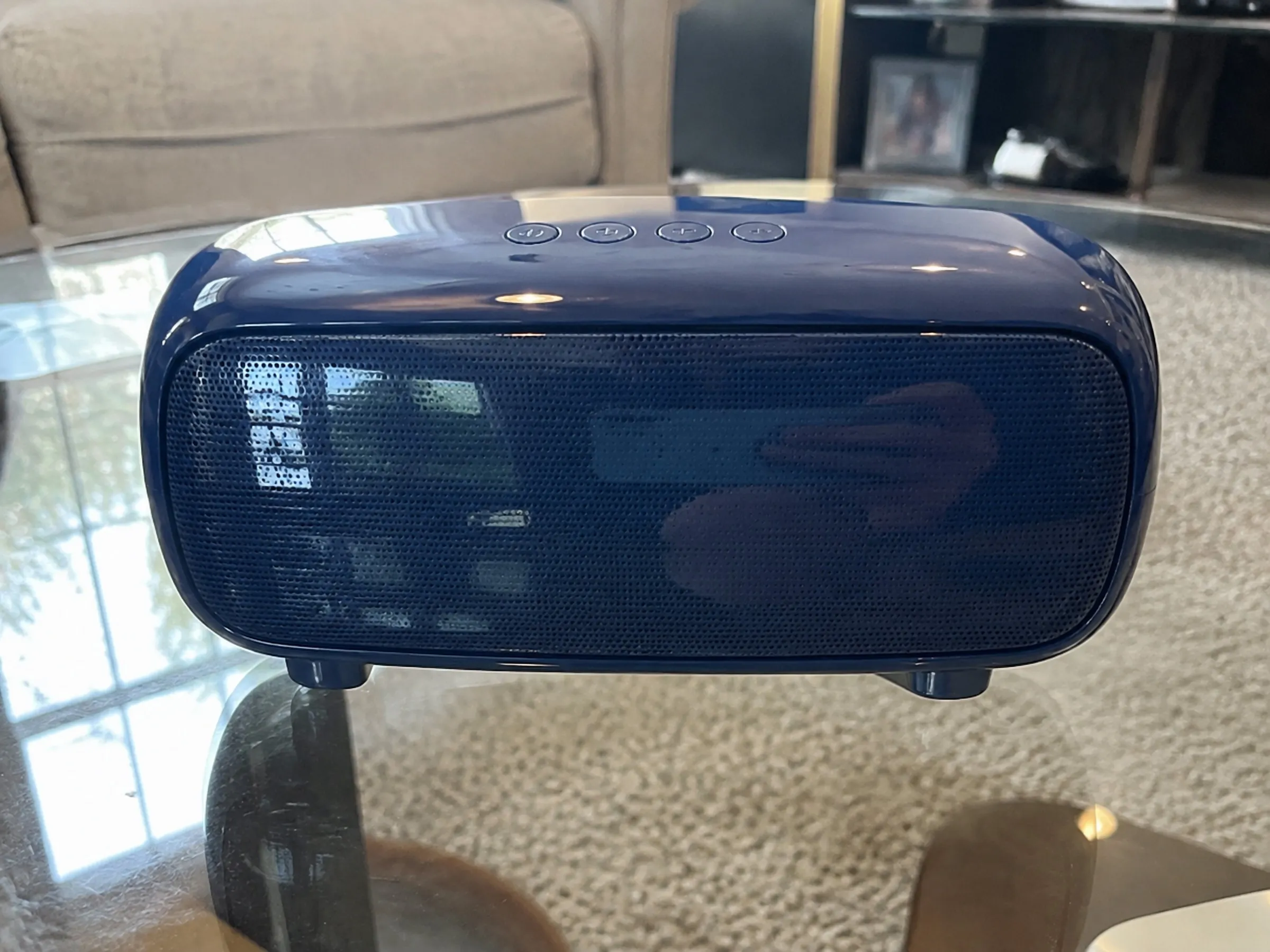 A navy bluetooth speaker photographed on a side table at home
