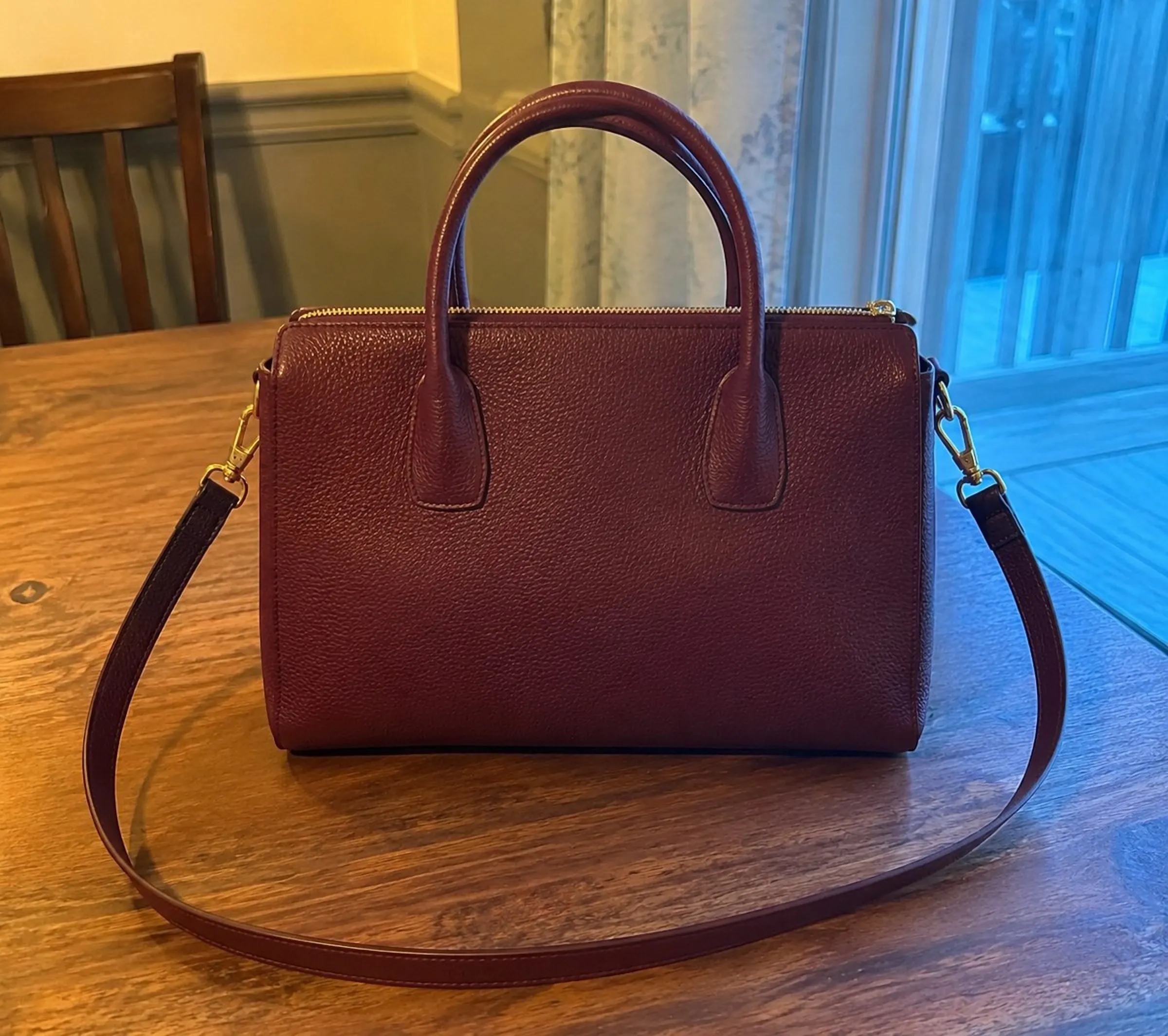 A burgundy leather satchel photographed on a dining table in evening light
