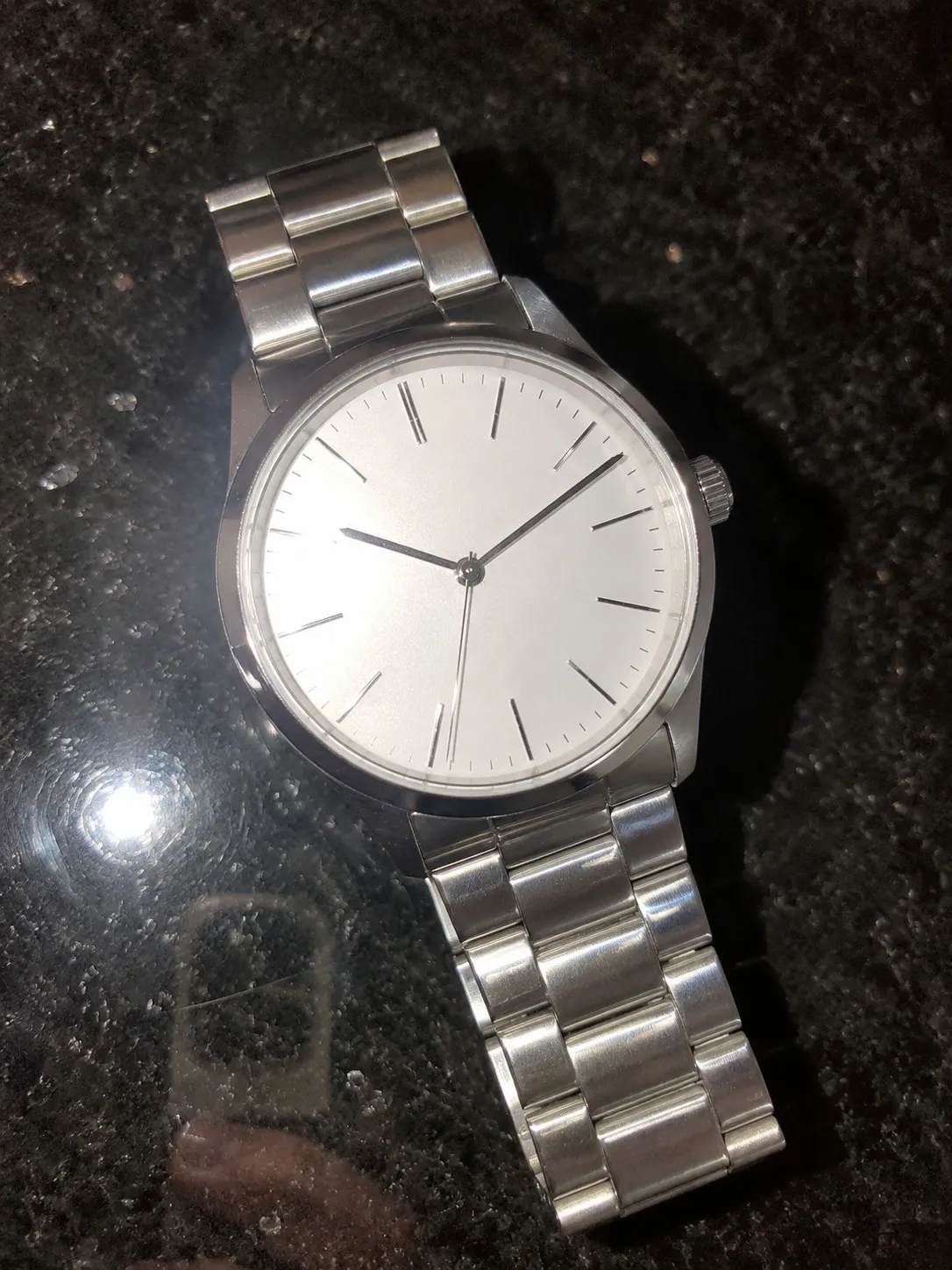 A steel wristwatch photographed on a dark granite counter, the flash reflected in the stone